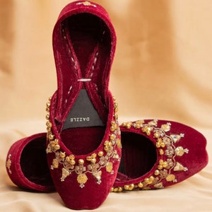 May include: A pair of maroon velvet shoes with gold embroidery and embellishments. The shoes have a pointed toe and a low heel. The brand name "DAZZLE" is visible on the inside of one shoe.