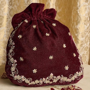 以下が含まれることがあります： ゴールドとピンクの花柄の刺繍とタッセルが付いた、マルーンのベルベット製の巾着袋。バッグはゴールドのビーズで飾られています。