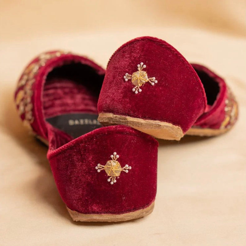 May include: A pair of burgundy velvet slippers with gold embroidery. The slippers have a pointed toe and a low heel. The embroidery features a geometric design with a central star.