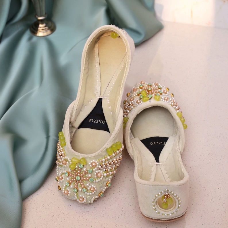 Pu&ograve; includere: Un paio di pantofole in velluto color avorio con perline e ricami intricati. Le pantofole presentano una gamma di colori verde e oro e la parola "DAZZLE" &egrave; stampata all'interno di ogni pantofola.