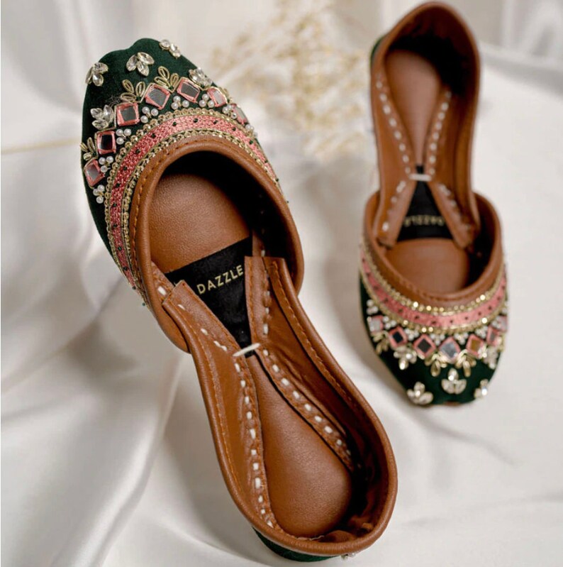 Puede incluir: Un par de zapatos de terciopelo verde con bordados rosa y dorados y adornos de espejo. Los zapatos tienen una plantilla de cuero marr&oacute;n y una punta puntiaguda. El nombre de la marca "DAZZLE" es visible en la plantilla.
