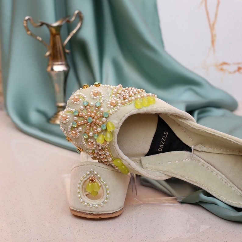 Pu&ograve; includere: Un paio di pantofole ricamate color crema con perline gialle e verdi. Le pantofole hanno un'etichetta del marchio Dazzle all'interno.