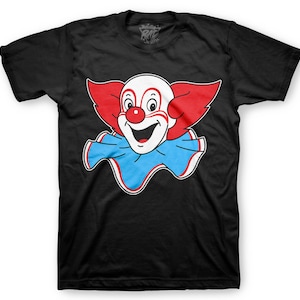 May include: Black t-shirt with a white and red cartoon clown face graphic. The clown has a big smile and blue collar.