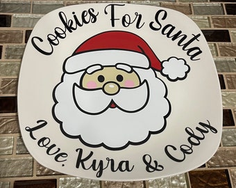 May include: White ceramic plate with a cartoon image of Santa Claus with the text "Cookies For Santa Love Kyra & Cody".
