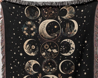 May include: A black woven throw blanket with a moon and flower design. The blanket features a repeating pattern of crescent moons and floral motifs in shades of gold and cream against a dark background. The blanket has a fringed edge.