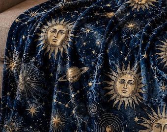 May include: A dark blue plush throw blanket featuring a celestial pattern with gold-toned illustrations of suns with faces, crescent moons, planets, and various star constellations scattered across the fabric surface in a repeating design.