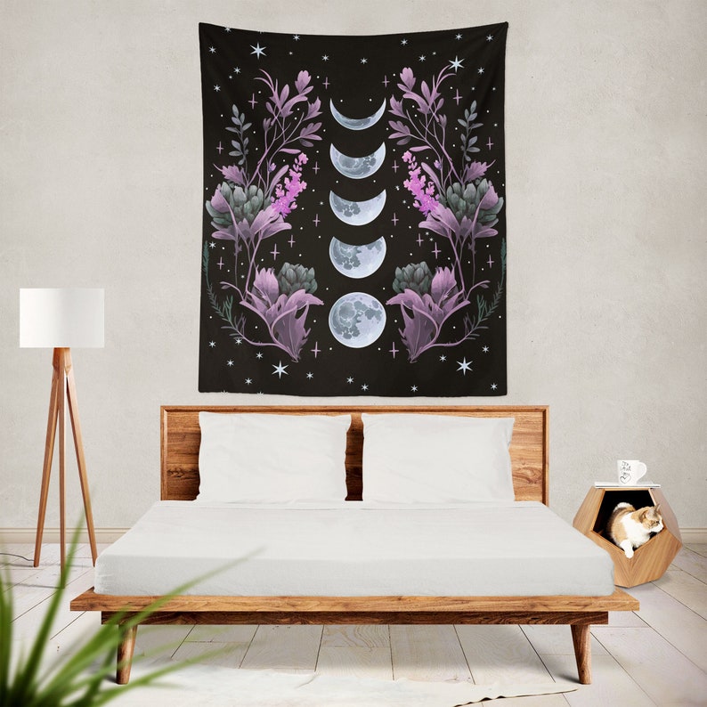 May include: A black tapestry with a floral design and a series of moons in different phases. The tapestry is hanging on a wall behind a bed with white bedding.
