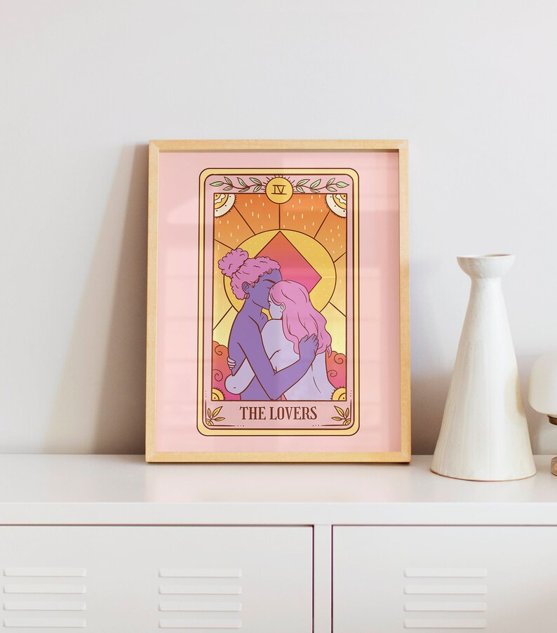 Op de afbeelding: Een ingelijste tarotkaart print met twee figuren die elkaar omarmen, met een roze achtergrond en een gouden rand. De kaart is gelabeld "THE LOVERS" en heeft een warm kleurenpalet met tinten roze, oranje en paars.