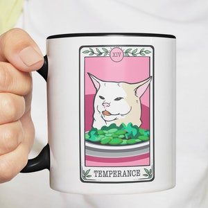 May include: White ceramic mug with a black rim and handle. The mug features a pink and white tarot card design with a white cat and the text "XIV TEMPERANCE".