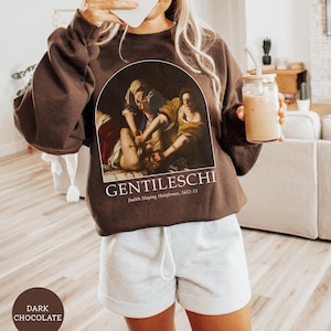 Peut inclure: Un sweat-shirt marron avec une peinture de Judith décapitant Holopherne par Artemisia Gentileschi. Le texte "Gentileschi" et "Judith décapitant Holopherne, 1612-13" est imprimé sous la peinture.