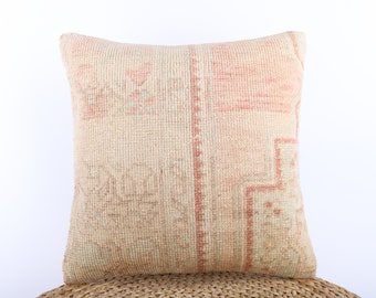 May include: A square throw pillow with a beige and pink woven pattern. The pillow has a subtle geometric design and a soft, textured surface.