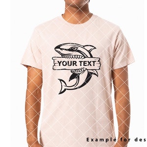 May include: A black and white illustration of a shark with its mouth open, biting a wooden sign that says "YOUR TEXT". The shark is on a light pink t-shirt.