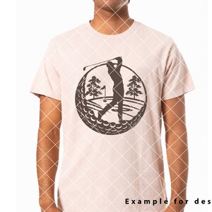 May include: A brown silhouette of a golfer swinging a club on a golf course, surrounded by a circle of golf balls. The design is on a light pink t-shirt.