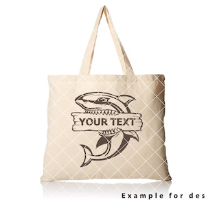 May include: A beige tote bag featuring a brown shark graphic and the text "YOUR TEXT" on a wooden sign. The shark is biting the sign.
