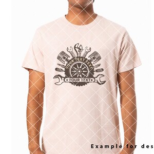 Op de afbeelding: Een lichtroze T-shirt met een bruin grafisch ontwerp van een band met gereedschap en de tekst "YOUR TEXT" twee keer herhaald.