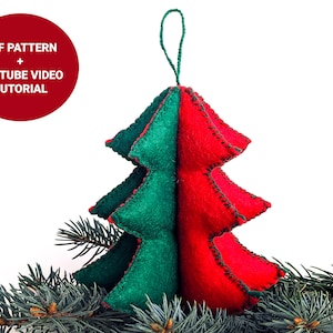 May include: A felt Christmas tree ornament with a red and green color scheme. The ornament is hanging from a green string and is surrounded by pine branches.