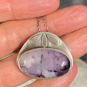 May include: A silver pendant with a purple and white agate stone set in a silver bezel. The pendant has a delicate chain and a design of four silver leaves.