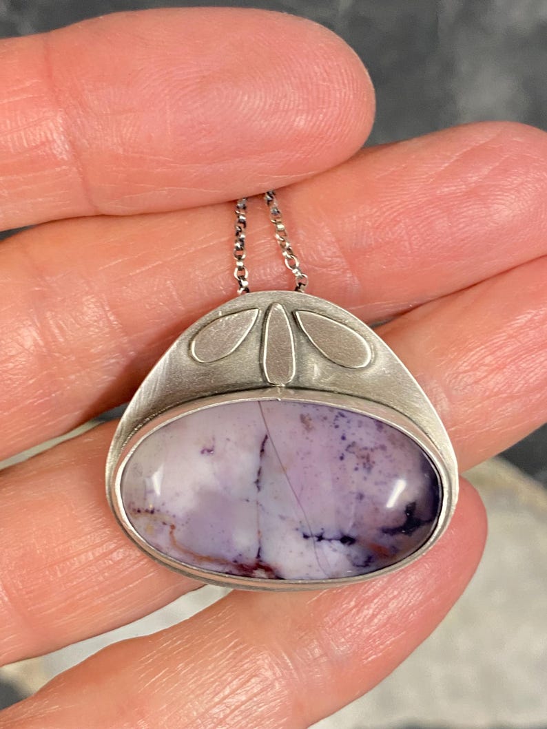 May include: A silver pendant with a purple and white agate stone set in a silver bezel. The pendant has a delicate chain and a design of four silver leaves.