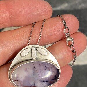 May include: A silver pendant necklace with a purple and white agate stone set in a silver bezel. The pendant has a delicate design with four small silver leaves around the stone.