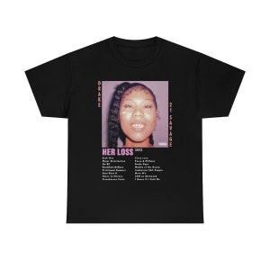 May include: Black t-shirt featuring a graphic of a woman's face with the text "HER LOSS 2022" and a list of song titles. The names "DRAKE" and "21 SAVAGE" are printed vertically on the sides of the graphic.