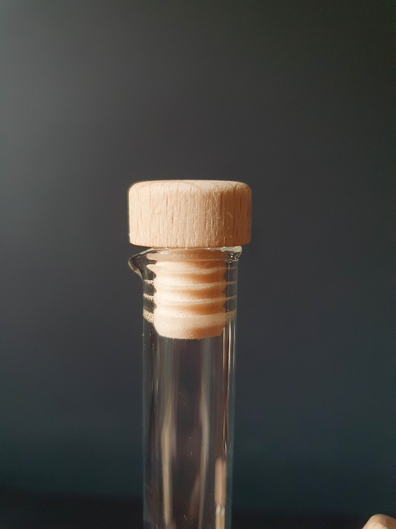 K&ouml;nnte beinhalten: Eine klare Glasflasche mit einem Stopfen aus Holz. Die Flasche ist leer und der Stopfen ist geschlossen.