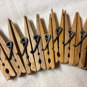 May include: A collection of wooden clothespins with dark metal springs. The clothespins are arranged in a row, showcasing their natural wood grain and classic design. The metal springs add a vintage touch to the laundry essentials.