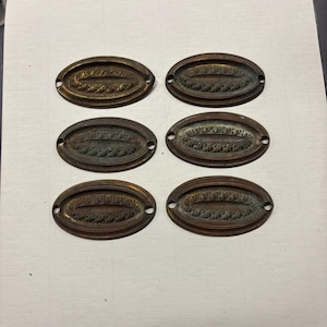 May include: Six antique oval-shaped brass drawer pulls with intricate floral designs. The pulls have a worn, aged patina and are ready to add a touch of vintage charm to any furniture project.