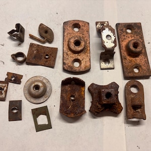 May include: A collection of various weathered metal hardware components, including rectangular plates, circular washers, and small brackets. These items exhibit significant rust, oxidation, and surface corrosion, showing a dark brown and metallic texture.