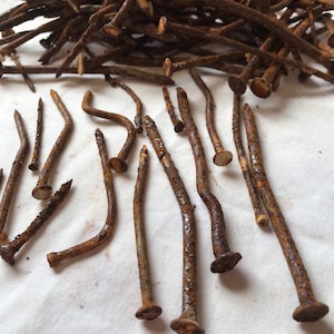 May include: A pile of rusty nails, some are bent and some are straight. The nails are on a white fabric surface.