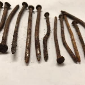 May include: A collection of rusty nails with various lengths and sizes. The nails are arranged in a semi-circle on a white surface.