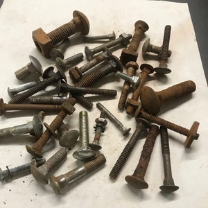 May include: A collection of rusty metal bolts and nuts with various sizes and shapes. Some of the bolts have a flat head and some have a round head. The bolts are all rusty and have a brown color.