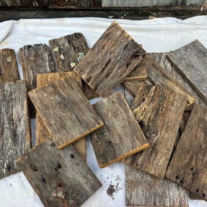 May include: A pile of reclaimed wood planks, weathered and worn with age, showing natural wood grain and knots. The planks are various sizes and shapes, with a rustic and distressed look.