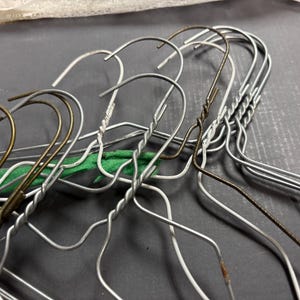 May include: A collection of vintage metal wire hangers. Some hangers have a silver finish, while others have a bronze or gold finish. Several hangers have a twisted wire design on the hook. A green fabric is visible between some of the hangers.