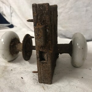 May include: Antique door knob with a white porcelain handle and a rusty metal base.