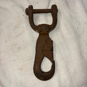 May include: A rusty metal hook with a D-ring and a screw closure. The hook is designed for attaching to a chain or rope.