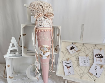 May include: A pink and floral-patterned school cone with a fox design. The cone is decorated with ribbons and pom-poms, and features the name "Mila" and the year "2023". The cone is part of a back-to-school theme.