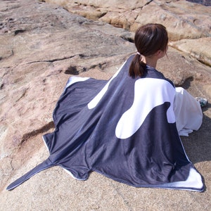 Puede incluir: Una persona lleva una capa con estampado de manta raya negra y blanca en una playa rocosa.