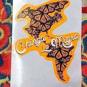 K&ouml;nnte beinhalten: Ein Aufkleber mit einer Weltkarte aus Monarchfaltern. Der Text "Chinga La Migra" ist in einer stilisierten Schrift geschrieben.