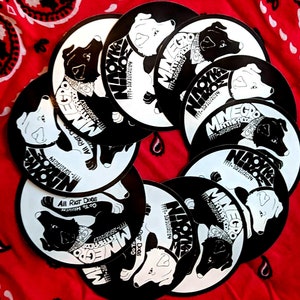 May include: A collection of black and white circular stickers featuring a dog with a bandana and the text "Minego" and "All Riot Dogs".