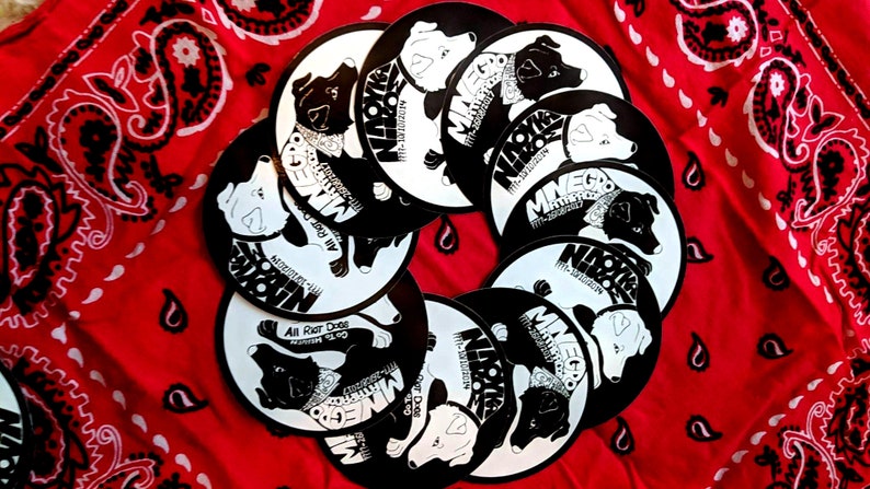 May include: A collection of black and white circular stickers featuring a dog with a bandana and the text "Minego" and "All Riot Dogs".