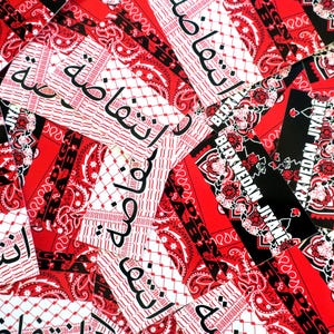K&ouml;nnte beinhalten: Eine Sammlung roter und schwarzer Bandanas und Aufkleber. Die Bandanas weisen ein Paisley-Muster und arabischen Text auf. Einige Aufkleber tragen den wei&szlig;en Text "BERXWEDAN JIYANE". Das Gesamtthema ist politischer Aktivismus.