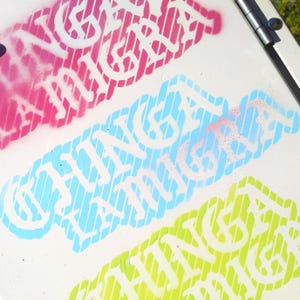 Puede incluir: Primer plano de tres dise&ntilde;os coloridos pintados con aerosol sobre una superficie blanca. Los dise&ntilde;os presentan el texto "CHING LANGA" en blanco, con cada palabra delineada en un color diferente: rosa, azul claro y verde. El fondo tiene l&iacute;neas diagonales.