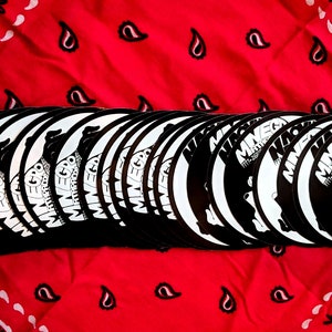 May include: A stack of black and white round stickers with the text "Mineg" and a graphic of a dog. The text "All Rat Dudes" is also visible on the sticker.