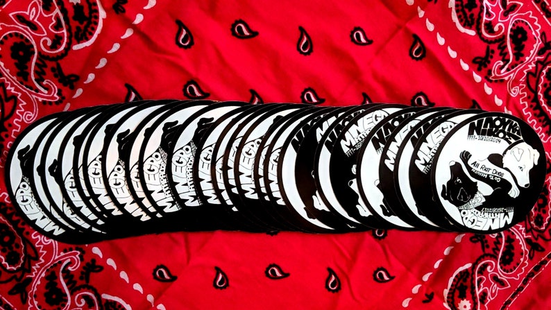 May include: A stack of black and white round stickers with the text "Mineg" and a graphic of a dog. The text "All Rat Dudes" is also visible on the sticker.