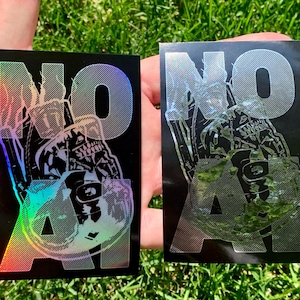 May include: Two rectangular black stickers featuring the text NO AI in a bold, diagonal-lined font. A stylized skull graphic is integrated into the letters. The left sticker displays a vibrant holographic finish, while the right sticker has a silver metallic finish.