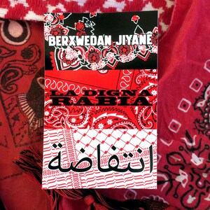 K&ouml;nnte beinhalten: Ein Stapel aus drei rot-wei&szlig;en Bandanas mit Text in Englisch und Arabisch. Das obere Bandana ist schwarz mit wei&szlig;en floralen Designs und dem Text "BERXWEDAN JIYANE". Das mittlere Bandana ist rot mit dem Text "LA DIGNA RABIA". Das untere Bandana ist wei&szlig; mit arabischem Text.