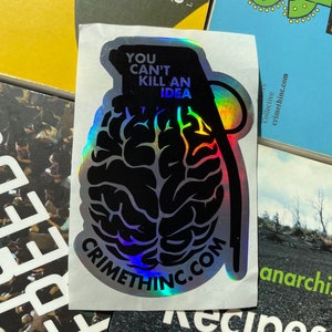 May include: A holographic sticker with a black and white image of a brain inside a grenade. The sticker has the text "You can't kill an idea" and "Crimethinc.com" on it.
