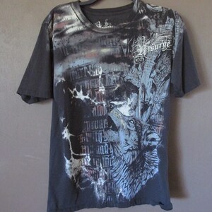 May include: A black short-sleeve t-shirt featuring a graphic print of a howling wolf in shades of blue and grey. The design includes gothic-style text, abstract patterns, and the word Resurge in a decorative white font across the upper right chest.