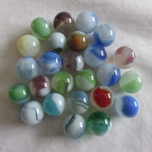 May include: A collection of colorful glass marbles in various sizes and designs. The marbles feature swirls of blue, green, red, white, and brown. Some marbles are translucent, while others are opaque. The marbles are scattered on a white surface.