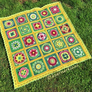 Può includere: Una coperta quadrata all'uncinetto caratterizzata da una griglia di motivi floreali e geometrici multicolori nelle tonalità del rosa, giallo, verde e blu, bordata da un bordo giallo con piccole nappe e il testo koernerklaus nell'angolo.